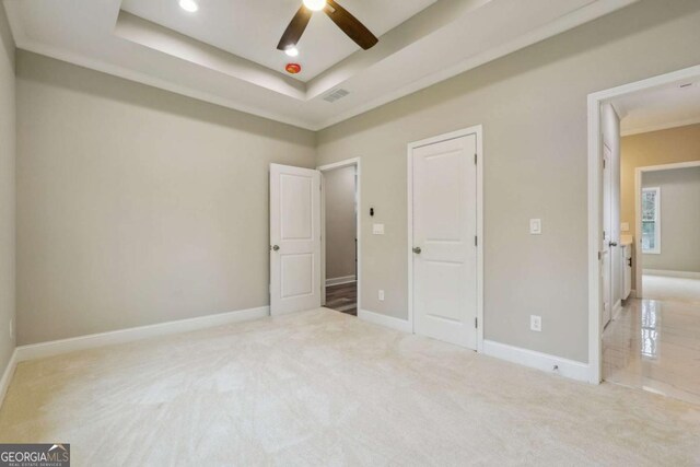 unfurnished bedroom with light colored carpet, a raised ceiling, and ceiling fan