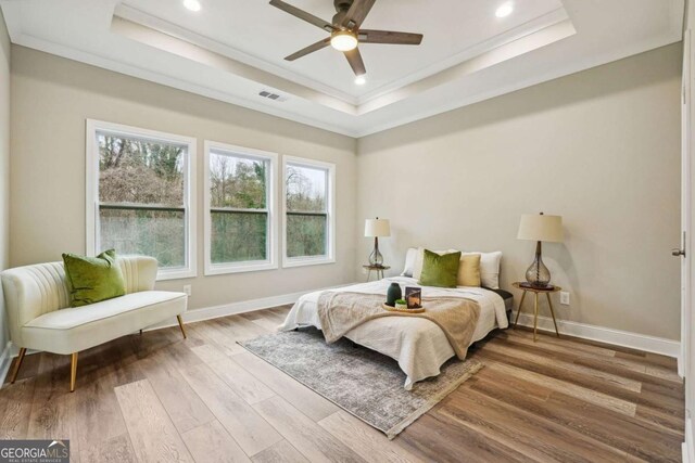 bedroom featuring a tray ceiling, ceiling fan, light hardwood / wood-style floors, and ornamental molding