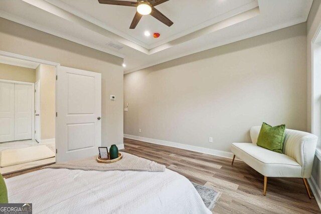 bedroom with light wood-type flooring, a raised ceiling, ceiling fan, and crown molding