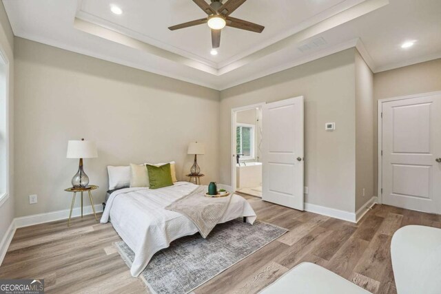 bedroom with ensuite bathroom, crown molding, ceiling fan, light wood-type flooring, and a tray ceiling