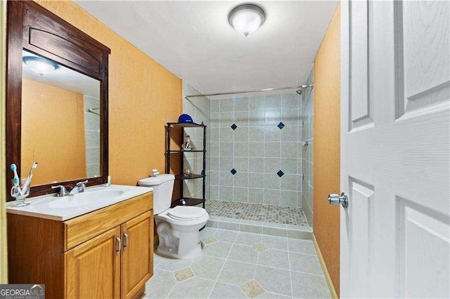 bathroom featuring tile patterned flooring, a tile shower, vanity, and toilet