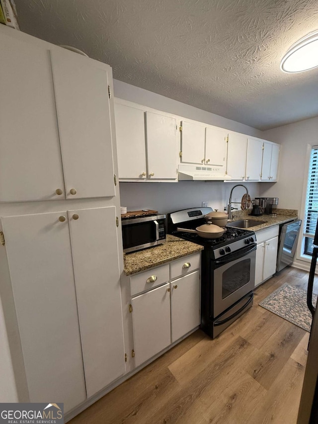 kitchen with sink, light hardwood / wood-style flooring, appliances with stainless steel finishes, light stone counters, and white cabinetry