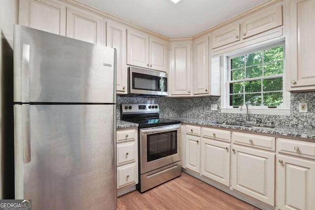 kitchen featuring light stone countertops, sink, backsplash, light hardwood / wood-style floors, and appliances with stainless steel finishes