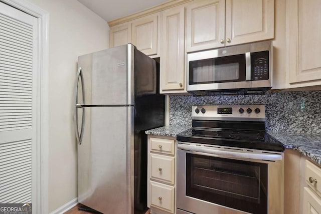 kitchen with backsplash, dark stone countertops, cream cabinetry, and appliances with stainless steel finishes