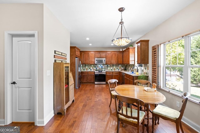 kitchen featuring sink, dark wood-type flooring, hanging light fixtures, decorative backsplash, and appliances with stainless steel finishes