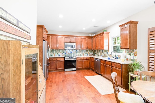 kitchen with tasteful backsplash, light stone counters, stainless steel appliances, sink, and light hardwood / wood-style floors