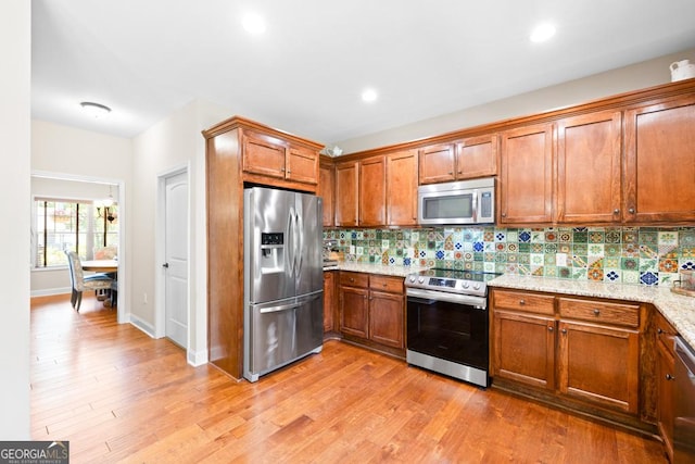 kitchen featuring backsplash, light stone counters, light hardwood / wood-style floors, and appliances with stainless steel finishes