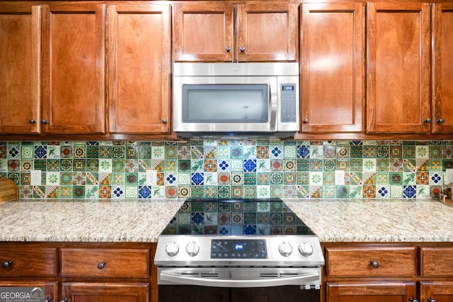 kitchen with light stone countertops, appliances with stainless steel finishes, and backsplash