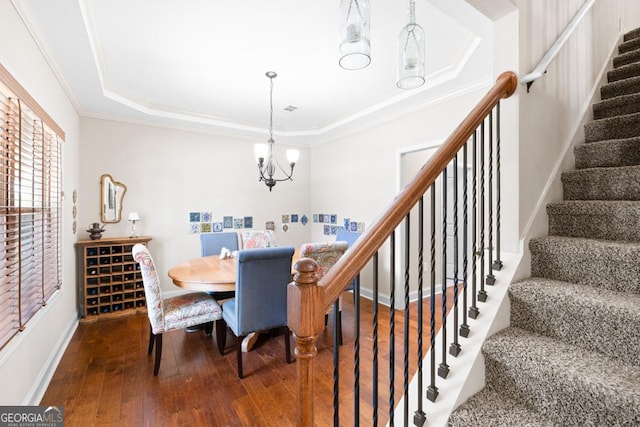 dining area with hardwood / wood-style flooring, an inviting chandelier, ornamental molding, and a tray ceiling