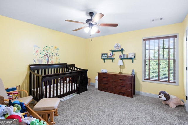 carpeted bedroom with ceiling fan and a nursery area