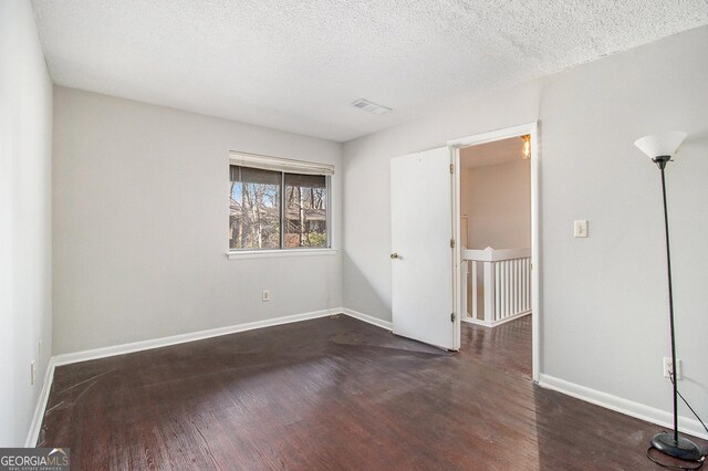 unfurnished room featuring dark wood-type flooring and a textured ceiling