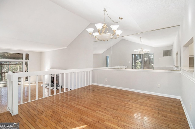 empty room with lofted ceiling, hardwood / wood-style flooring, and a chandelier