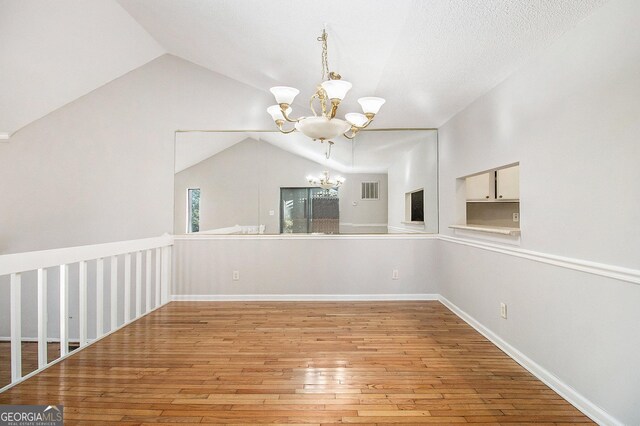 empty room with lofted ceiling, hardwood / wood-style floors, and an inviting chandelier