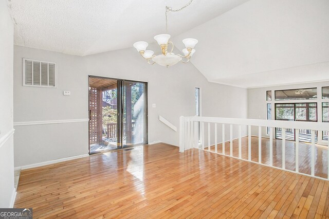 unfurnished room with vaulted ceiling, hardwood / wood-style floors, a textured ceiling, and a notable chandelier