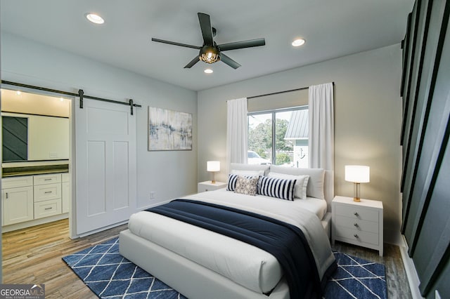 bedroom featuring hardwood / wood-style flooring, ceiling fan, and a barn door