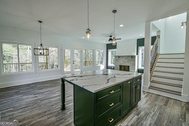 kitchen with french doors, ceiling fan with notable chandelier, a stone fireplace, a kitchen island, and light stone counters