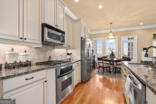 kitchen featuring appliances with stainless steel finishes, ornamental molding, sink, decorative light fixtures, and an inviting chandelier