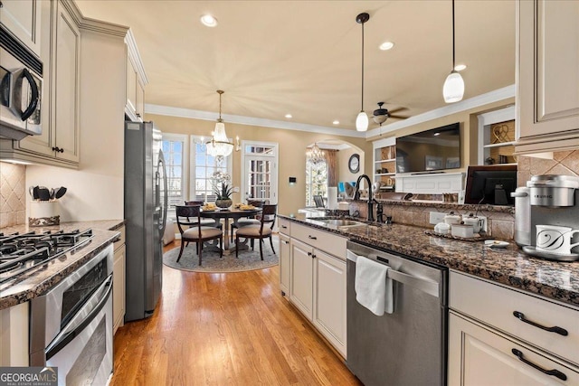 kitchen with sink, hanging light fixtures, crown molding, dark stone counters, and appliances with stainless steel finishes