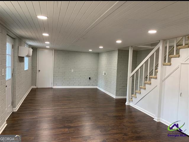 basement featuring wooden ceiling, dark hardwood / wood-style flooring, and brick wall