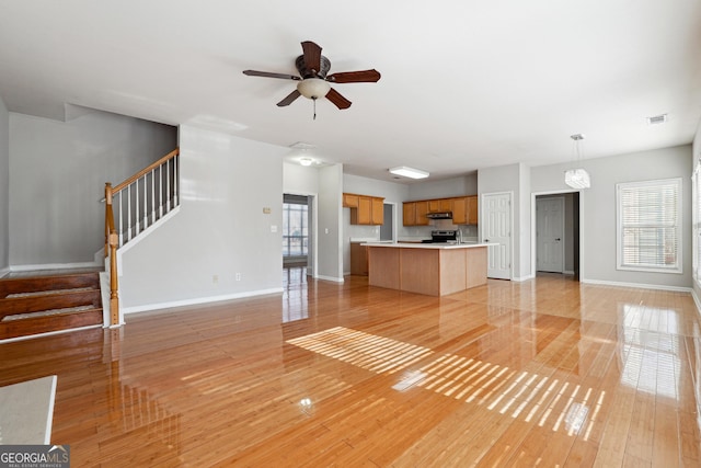 unfurnished living room featuring ceiling fan with notable chandelier and light hardwood / wood-style floors