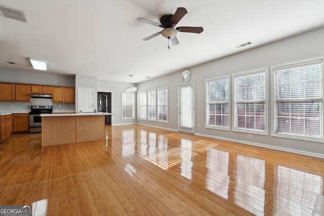 kitchen with ceiling fan, a kitchen island with sink, a healthy amount of sunlight, and stainless steel electric range