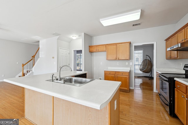 kitchen with a center island with sink, black electric range oven, light wood-type flooring, and sink