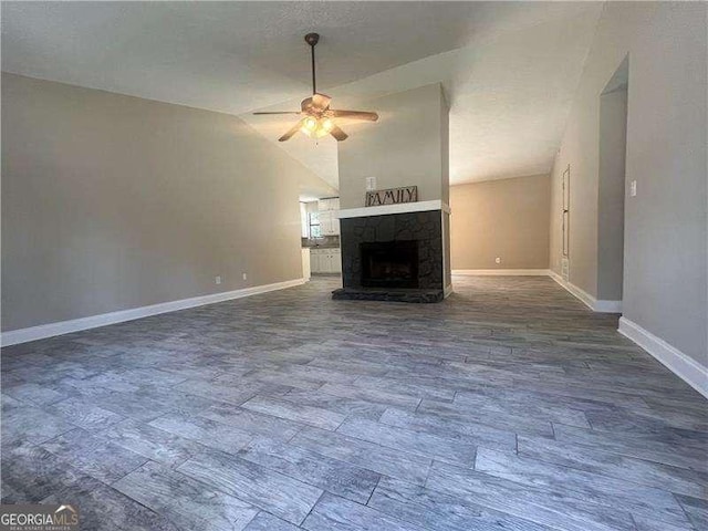 unfurnished living room with vaulted ceiling, a stone fireplace, and ceiling fan