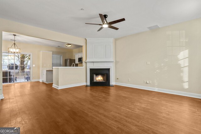 unfurnished living room with ceiling fan with notable chandelier, a fireplace, and dark wood-type flooring