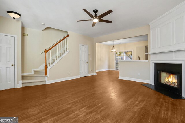 unfurnished living room featuring ceiling fan with notable chandelier and dark wood-type flooring