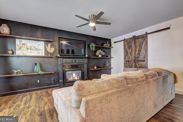 living room with a barn door, a fireplace, ceiling fan, and dark wood-type flooring