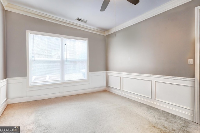 spare room with a wainscoted wall, crown molding, light colored carpet, visible vents, and a ceiling fan