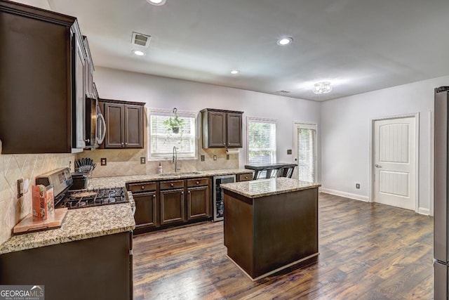 kitchen featuring light stone countertops, appliances with stainless steel finishes, a sink, and a center island