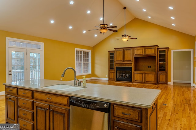 kitchen featuring light wood-type flooring, stainless steel dishwasher, sink, high vaulted ceiling, and an island with sink