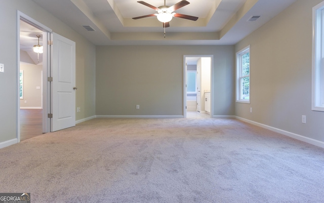 unfurnished room with ceiling fan, a raised ceiling, and light colored carpet