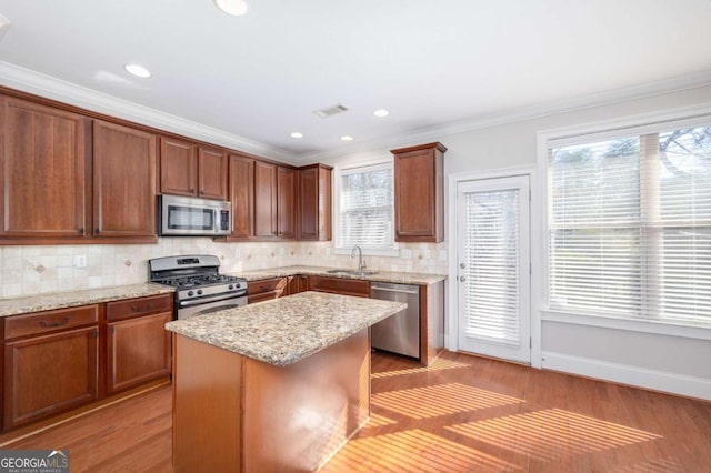 kitchen with light hardwood / wood-style floors, ornamental molding, appliances with stainless steel finishes, a kitchen island, and light stone counters