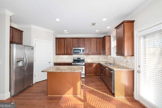 kitchen with appliances with stainless steel finishes, light stone counters, ornamental molding, sink, and a center island