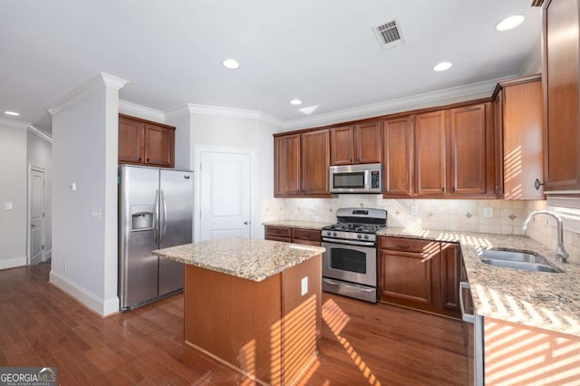 kitchen with sink, light stone countertops, ornamental molding, a kitchen island, and stainless steel appliances