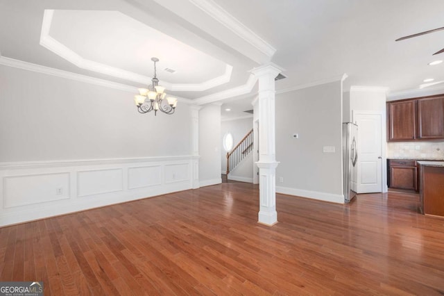 interior space with an inviting chandelier, a raised ceiling, ornamental molding, dark hardwood / wood-style flooring, and decorative columns