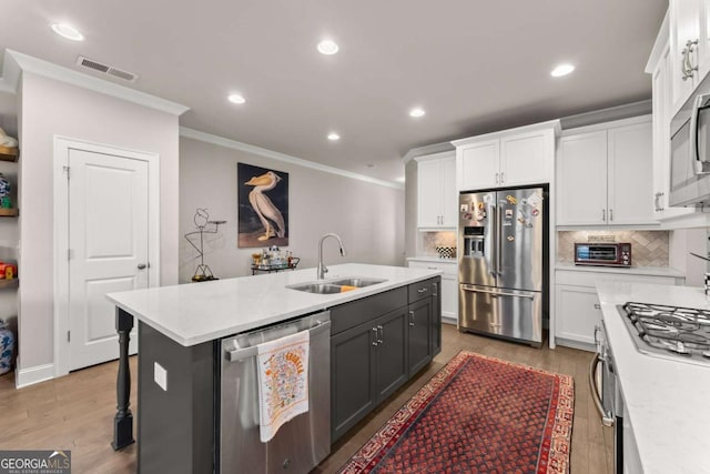 kitchen with ornamental molding, stainless steel appliances, sink, white cabinetry, and an island with sink