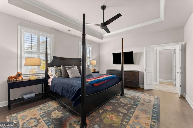 bedroom with hardwood / wood-style floors, ceiling fan, and a raised ceiling