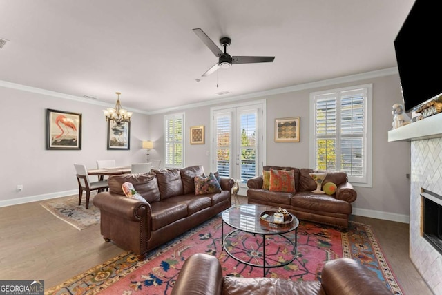 living room with hardwood / wood-style flooring, ceiling fan with notable chandelier, crown molding, and a fireplace