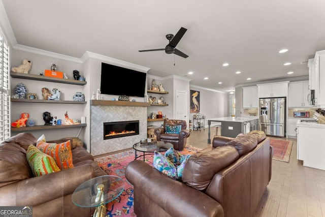 living room with a tile fireplace, light hardwood / wood-style flooring, ceiling fan, and ornamental molding