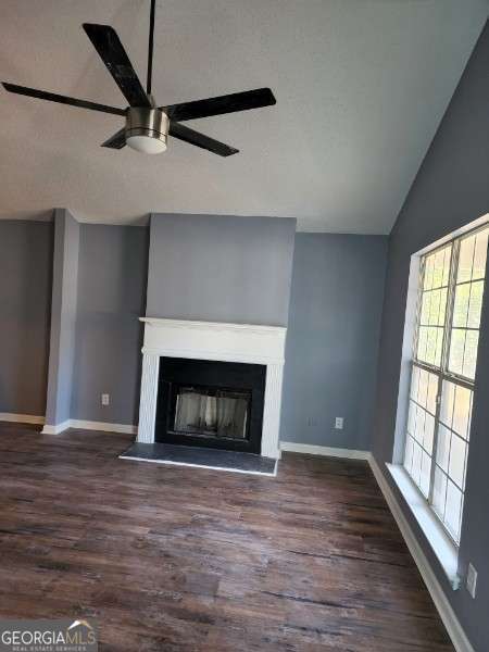 unfurnished living room featuring ceiling fan, dark hardwood / wood-style floors, and vaulted ceiling