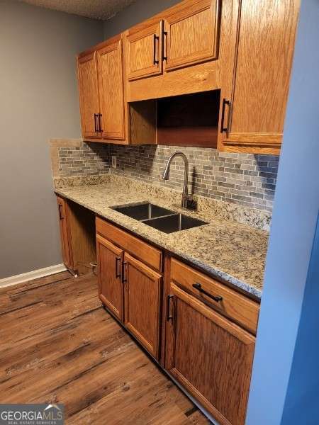 kitchen with hardwood / wood-style floors, light stone counters, sink, and tasteful backsplash