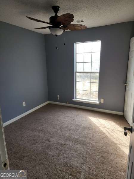 carpeted spare room featuring ceiling fan and a textured ceiling