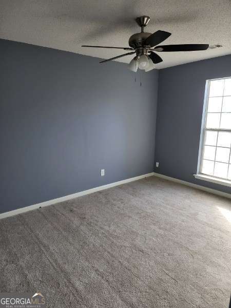 carpeted empty room featuring ceiling fan and a textured ceiling