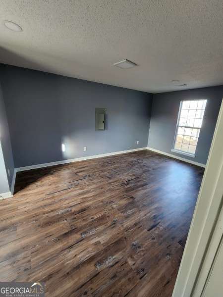 empty room with dark hardwood / wood-style floors, a textured ceiling, and electric panel