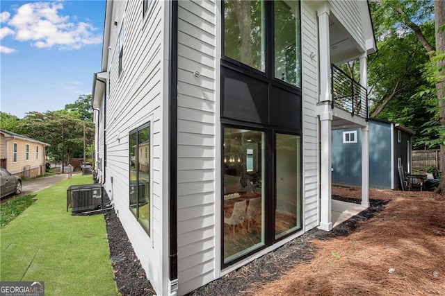 view of side of home with central air condition unit, a yard, and a balcony