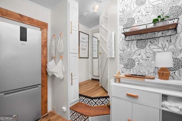 interior space with white cabinetry, stainless steel refrigerator, and ornamental molding