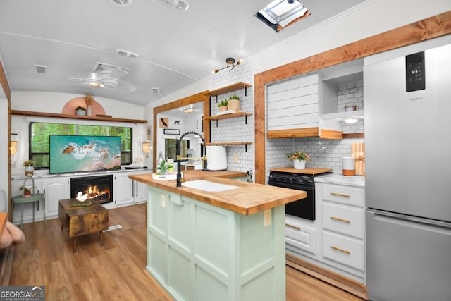 kitchen with butcher block counters, sink, stainless steel fridge, vaulted ceiling, and white cabinets